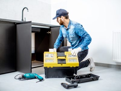 Handyman in blue shirt and cap mounting or repairing kitchen furniture in the apartment
